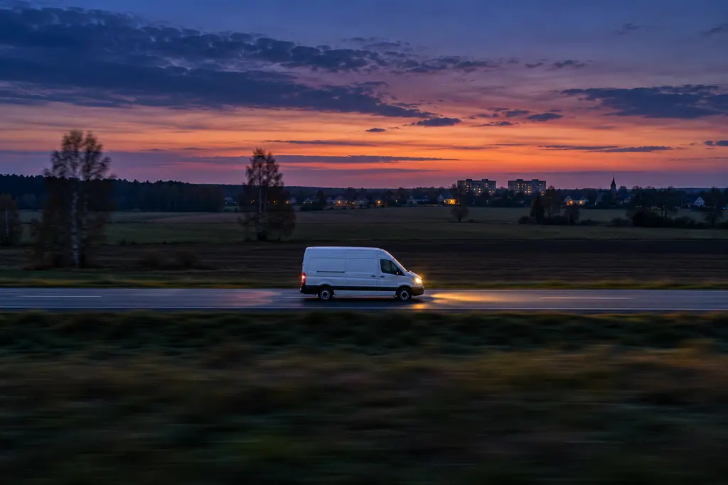 A white van driving along a country road at dusk